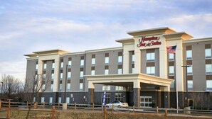 A Hampton Inn & Suites hotel with a modern facade, large windows, and an American flag.