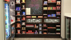 A snack display area with various packaged snacks and a chalkboard with a Valentine's Day message.