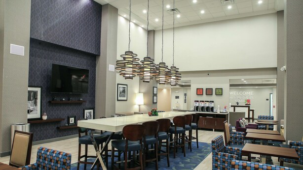 A modern hotel lobby with a central bar area, seating arrangements, and a 'Welcome to the Garden State' sign.
