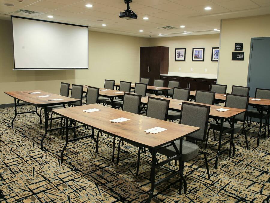 A conference room with a large projection screen, multiple tables, and chairs.