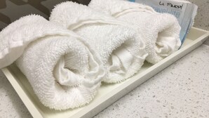 Un plateau blanc contenant des serviettes pliées avec soin et un ensemble de serviettes de toilette La Fresh, en format voyage.
