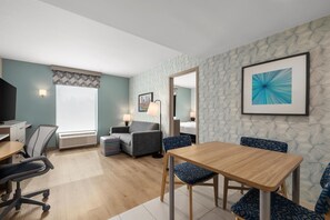Une chambre d’hôtel comprenant un coin repas, un canapé, un fauteuil, un bureau et un téléviseur.