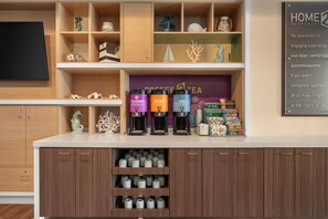 Un espace d’accueil d’hôtel comprenant un coin café, un panneau indiquant « GARANTIE CONFORT » et divers objets décoratifs disposés sur des étagères.