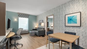 A modern hotel room with a desk, office chair, sofa, and dining table.