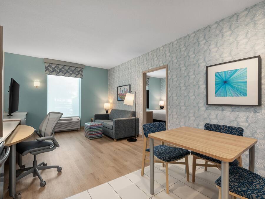 Una habitación de hotel moderna con escritorio, silla de oficina, sofá y mesa de comedor.