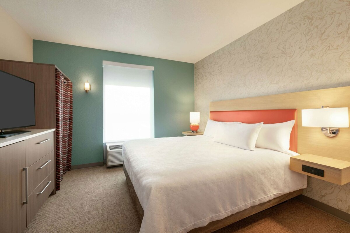 A hotel room with a bed, a TV, a desk, and a window.
