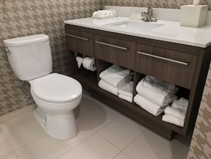 A bathroom with a toilet, a sink, and a vanity with towels.