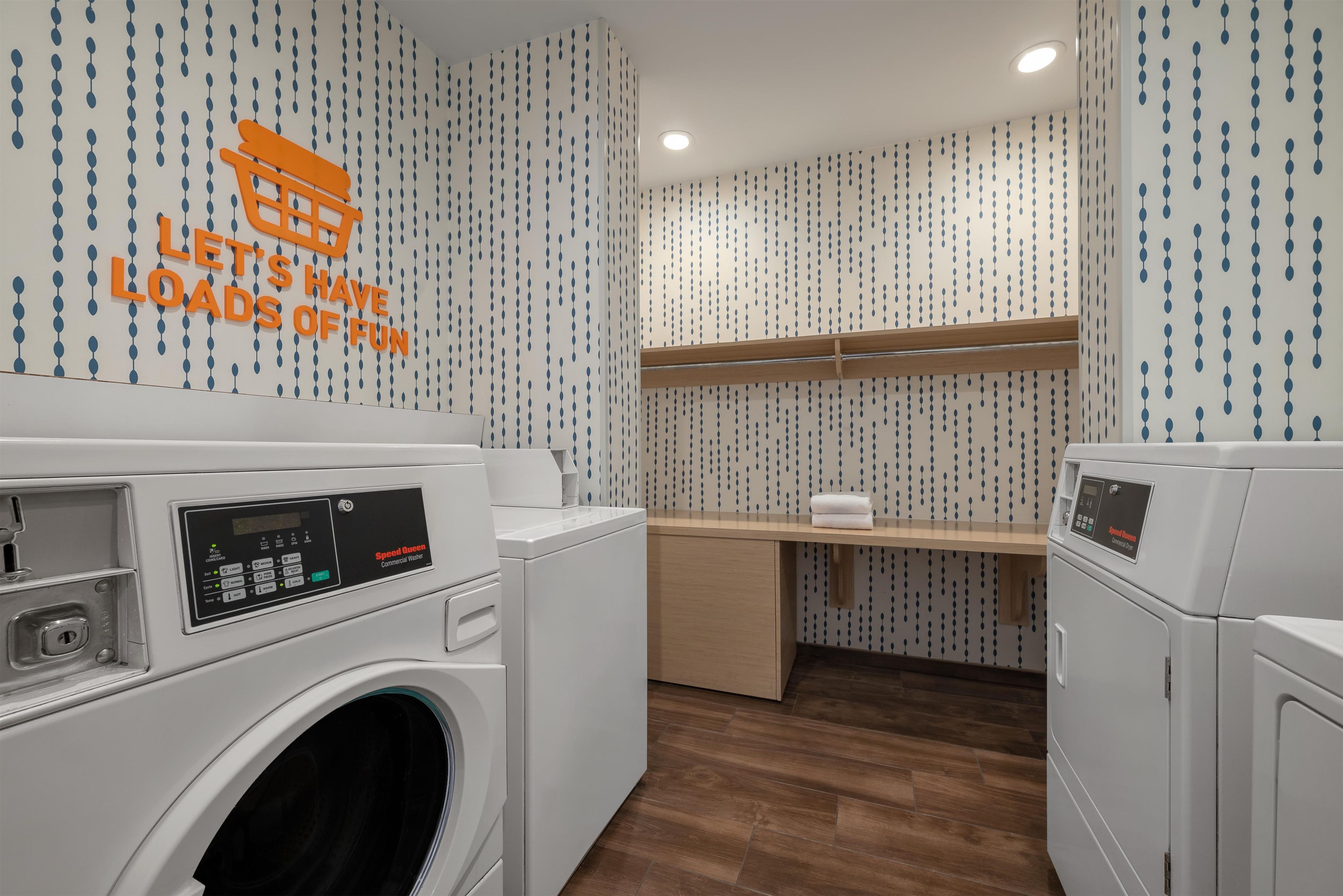 A laundry room with two front-loading washing machines, a wooden shelf, and a wall with a pattern of blue and white teardrop shapes.