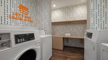 A laundry room with two front-loading washing machines, a wooden shelf, and a wall with a pattern of blue and white teardrop shapes.