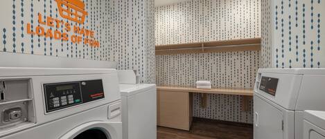 A laundry room with two front-loading washing machines, a wooden shelf, and a wall with a pattern of blue and white teardrop shapes.