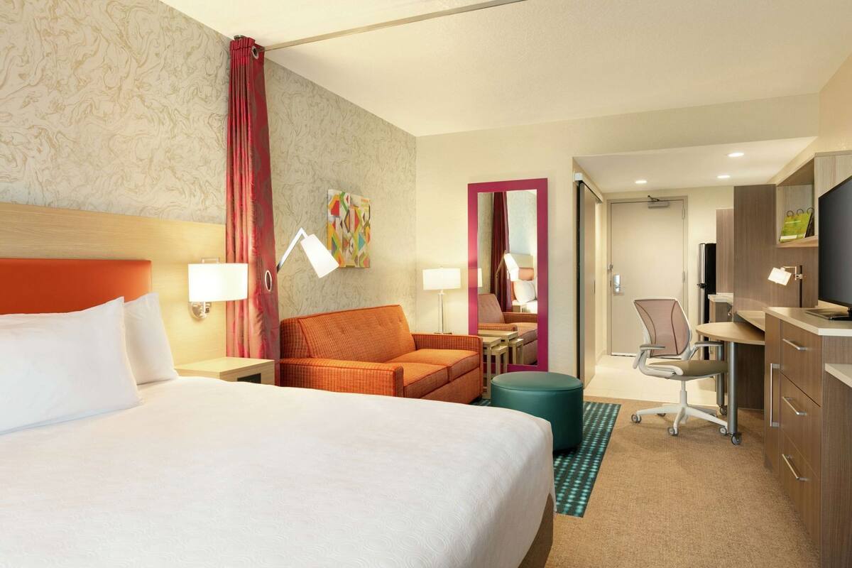 Een hotelkamer met een bed, een bureau, een stoel, een klein tafeltje, een spiegel en een televisie.