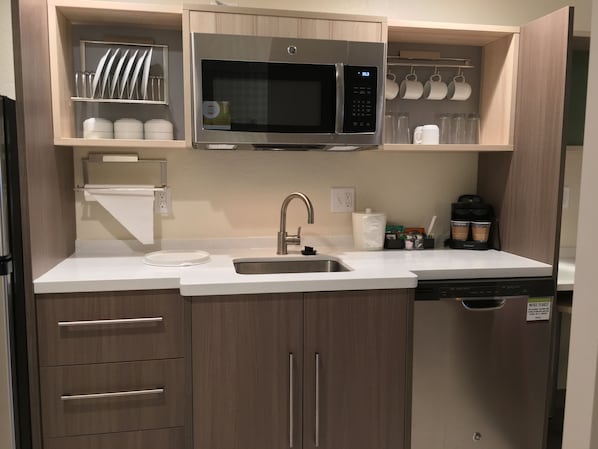 A modern kitchen with a stainless steel microwave, a sink, and wooden cabinets.