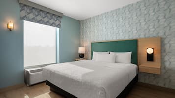 A hotel room with a large bed, a nightstand with a lamp, a wall-mounted light, and a window with a patterned curtain.