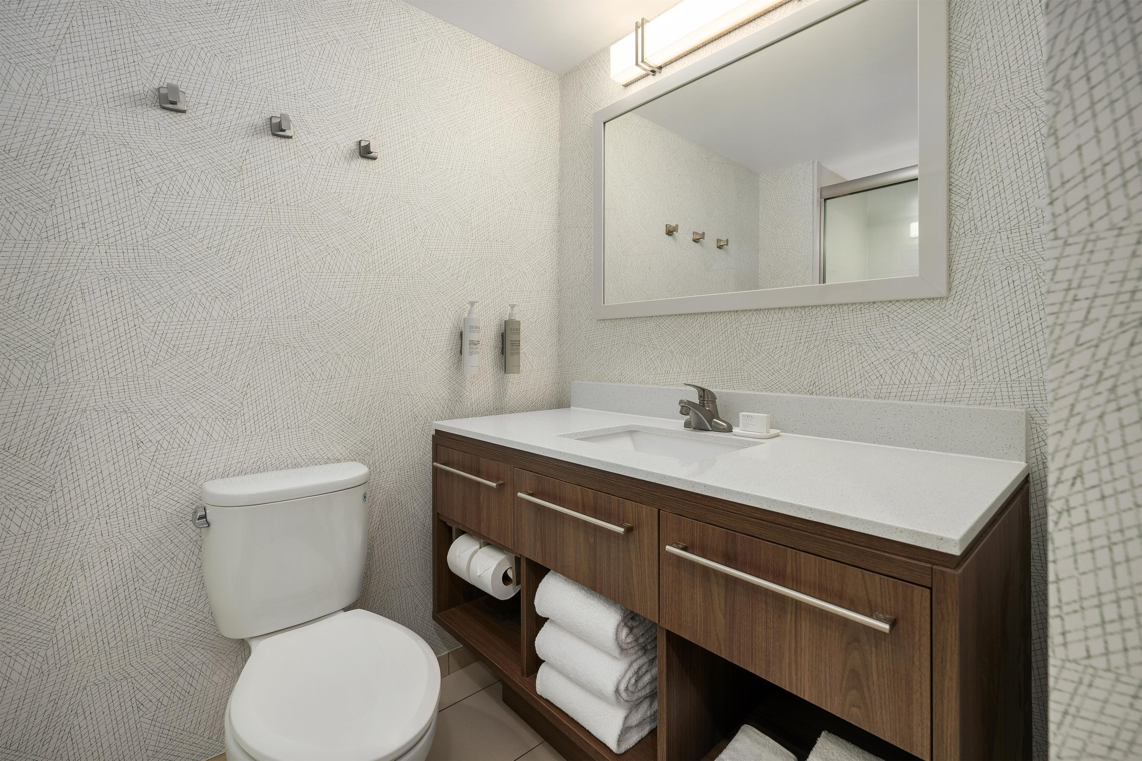 A modern bathroom with a white toilet, a wooden vanity with a mirror, and a towel rack.