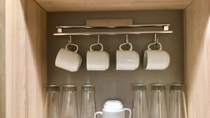 Un meuble en bois avec une étagère où sont posées des tasses blanches et des verres transparents.