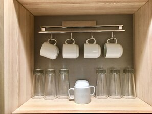 A wooden cabinet with a shelf holding white mugs and clear glasses.