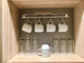 Un gabinete de madera con un estante que contiene tazas blancas y vasos de vidrio.
