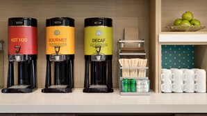 Trois machines à café étiquetées « EAU CHAUDE », « GOURMET » et « DÉCAFÉINÉ » sont posées sur un comptoir.