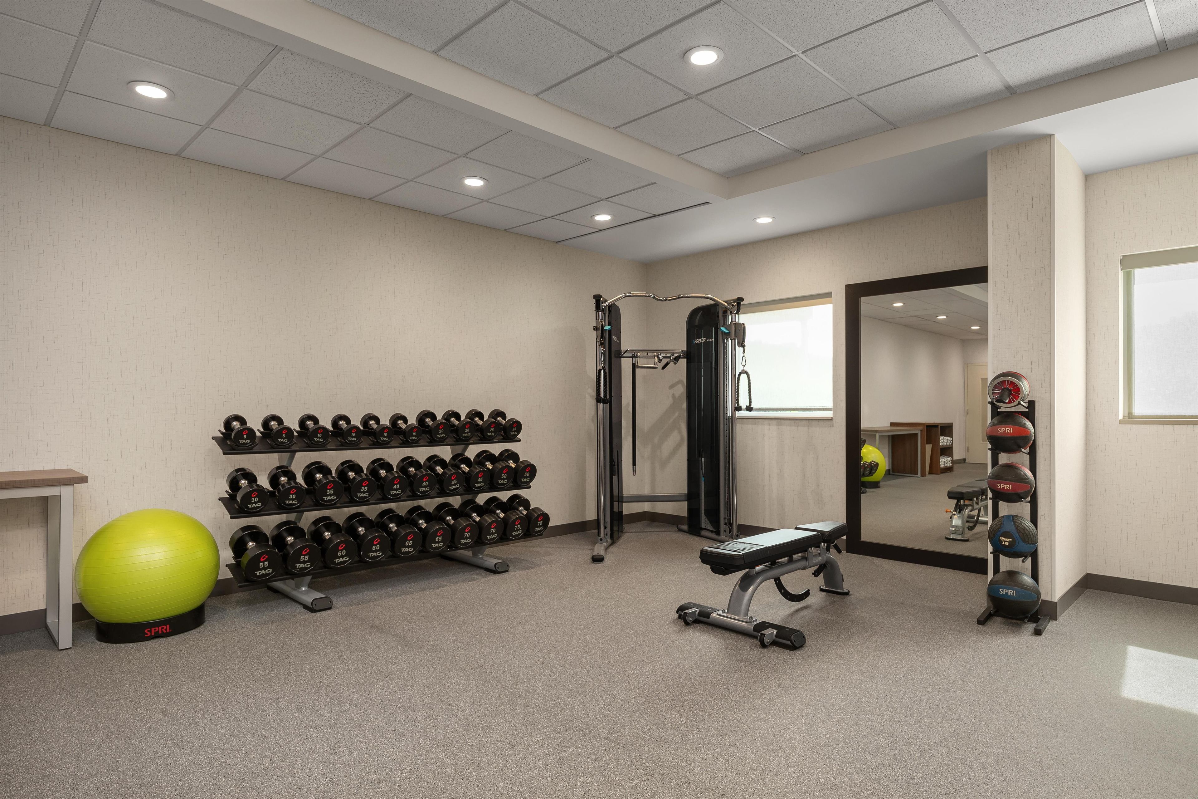 A gym with weightlifting equipment, a mirrored wall, and a green exercise ball.