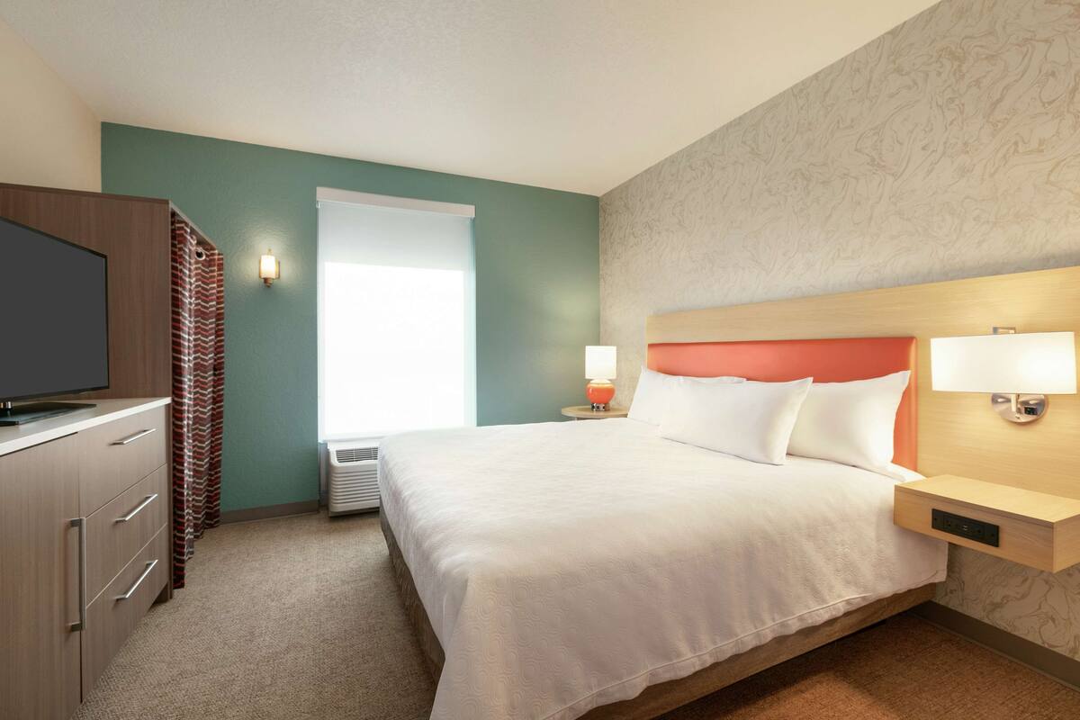 Een hotelkamer met een bed, een televisie, een nachtkastje met een lamp en een raam met gordijnen.