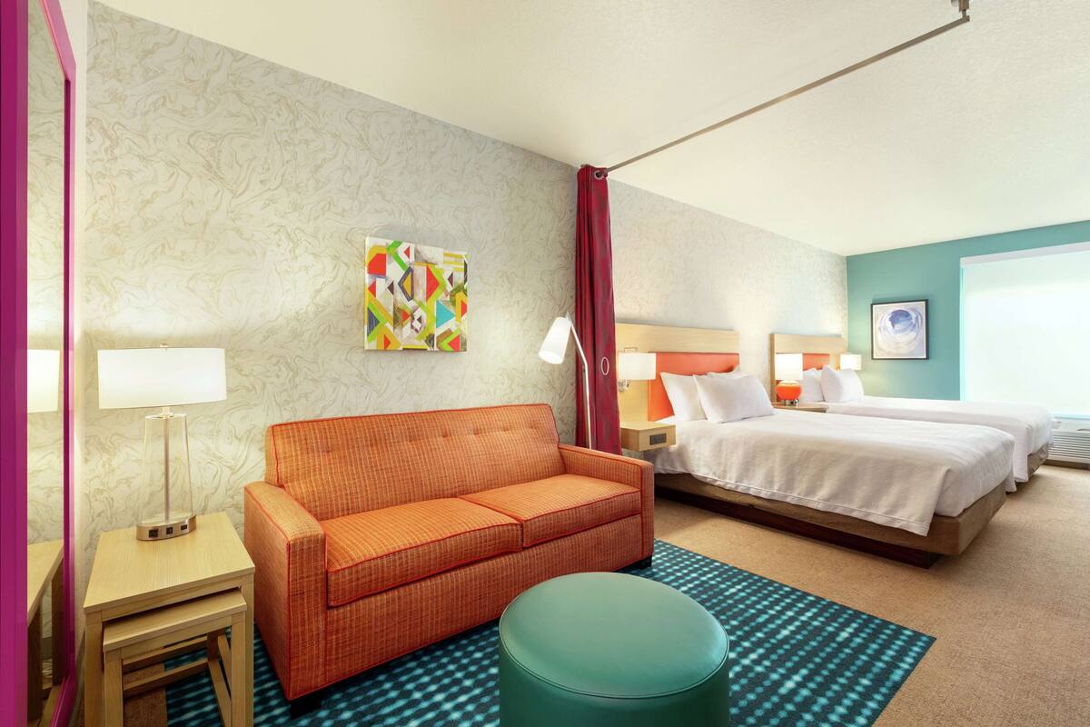 Een hotelkamer met een bed, een bank, een klein tafeltje, een lamp en een kleurrijk kunstwerk aan de muur.