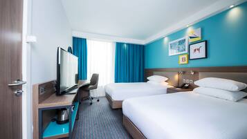 A hotel room with two beds, a desk with a television, a chair, and a minibar.