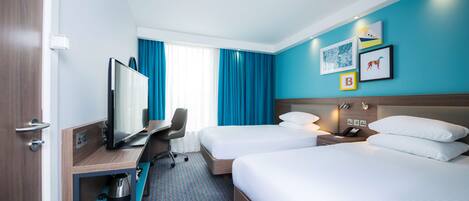A hotel room with two beds, a desk with a television, a chair, and a minibar.