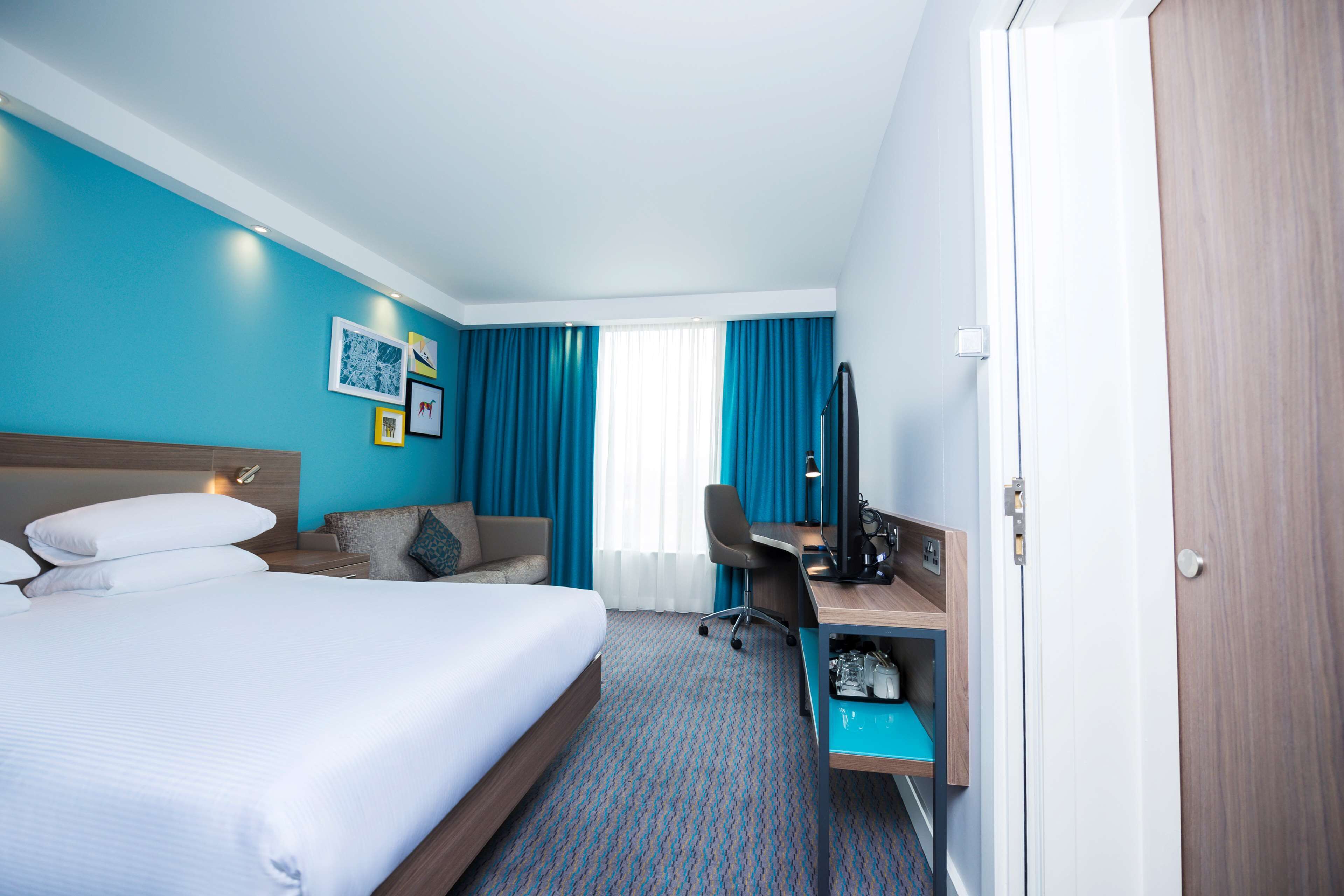 A hotel room with a bed, a desk, a chair, and a TV.
