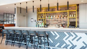 A bar area with a modern design, featuring a brick wall, a yellow metal shelf, and multiple hanging lights.