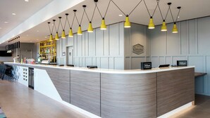 A modern hotel reception area with a curved counter, multiple receptionists' stations, a minibar, and a bar area.