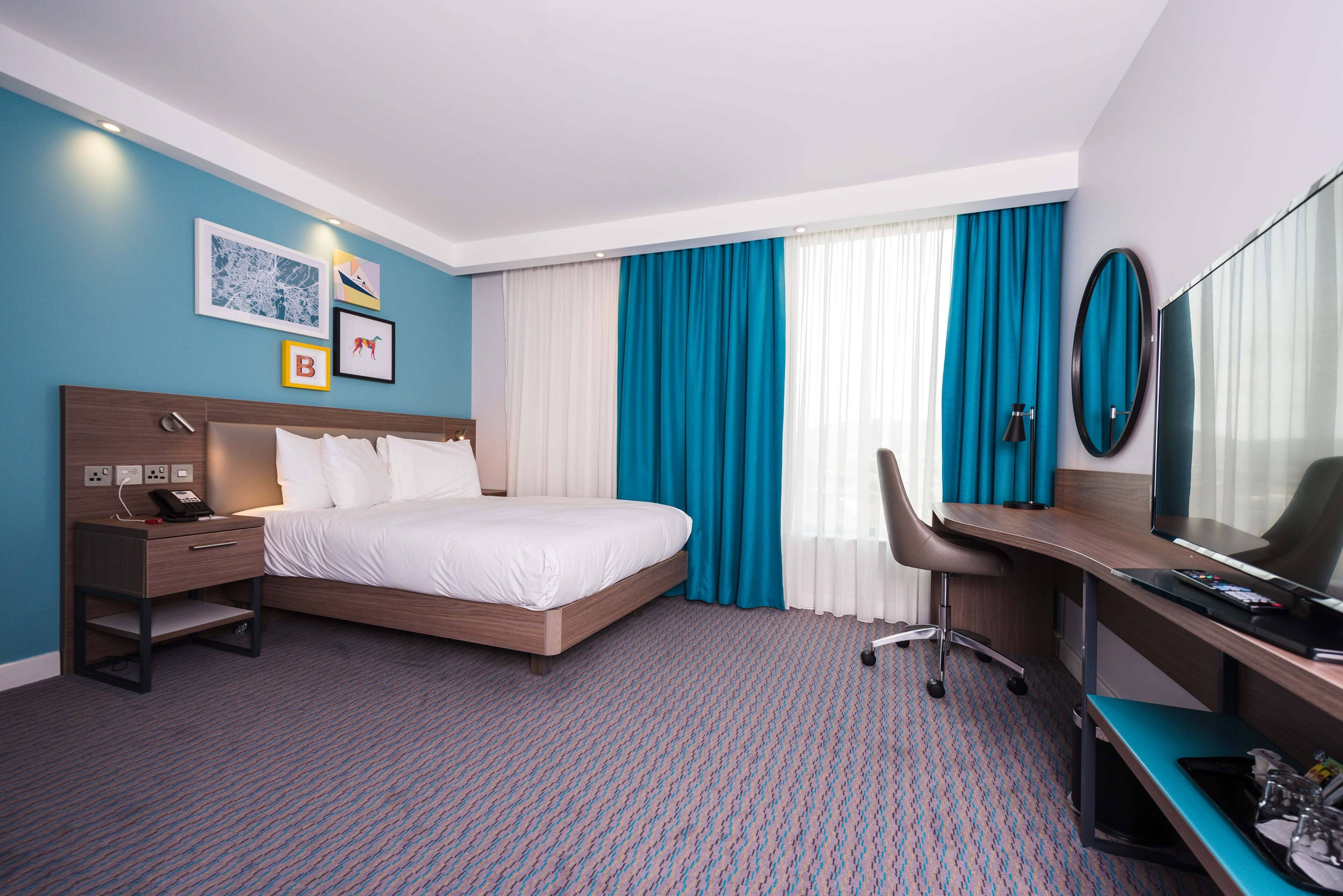 Una habitación de hotel con cama, escritorio, silla y televisor.