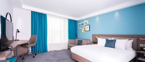 A hotel room with a large bed, a desk with a chair, a TV, and a window with curtains.