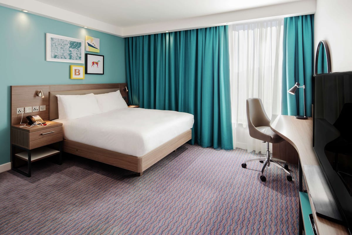 Une chambre d’hôtel comprenant un lit, un bureau avec une chaise, une télévision et une lampe de bureau.