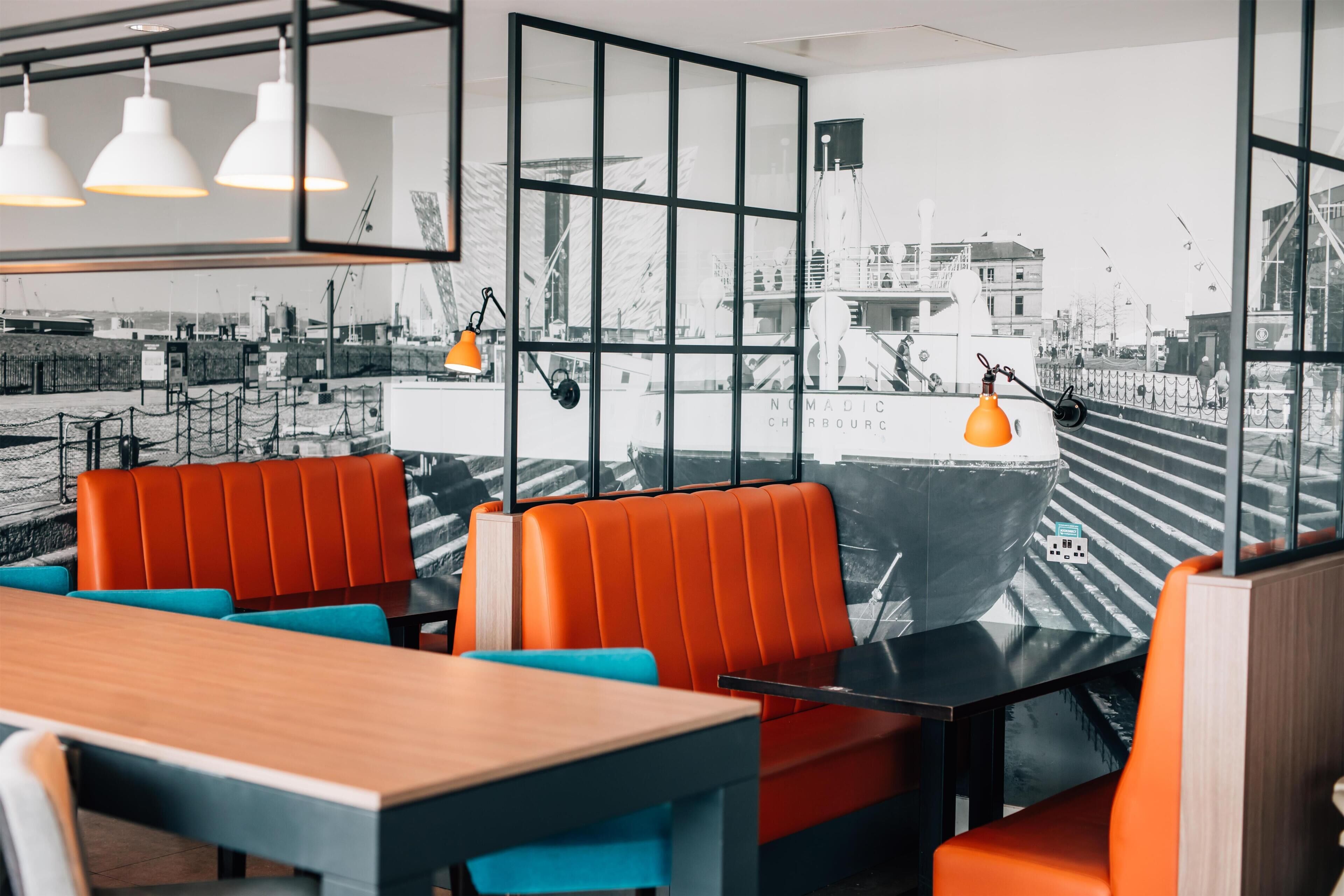 Een restaurant met uitzicht op een schip door grote ramen, met oranje en blauwe zitplaatsen.