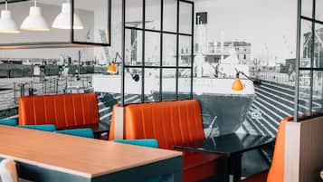 A restaurant with a view of a ship through large windows, featuring orange and blue seating.