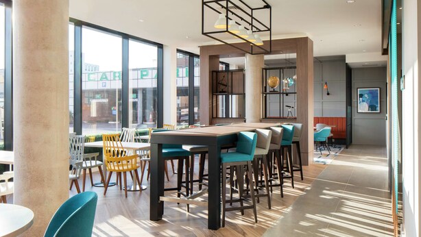 A modern dining area with high ceilings, large windows, and a mix of bar and table seating.