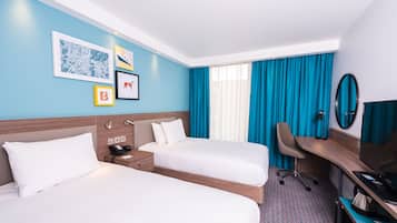 A hotel room with two beds, a desk, a chair, a TV, and artwork on the wall.