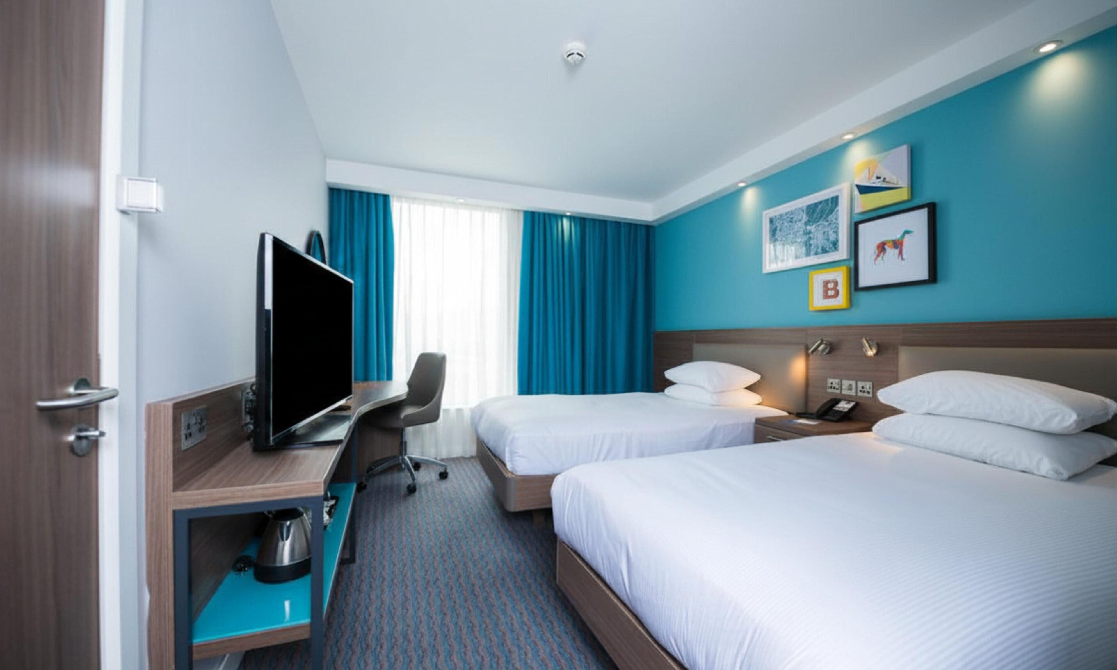 A hotel room with two beds, a desk with a flat-screen TV, a chair, and a coffee maker.