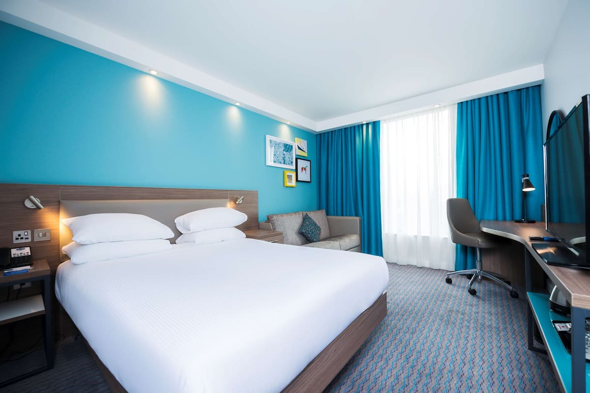 Une chambre d’hôtel avec un grand lit, un bureau avec une chaise, un canapé et un téléviseur.