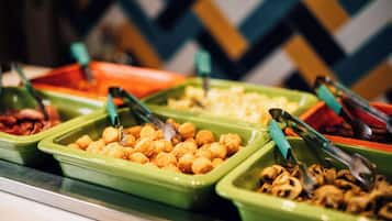 A buffet with various food options in green and orange containers, including tongs for serving.