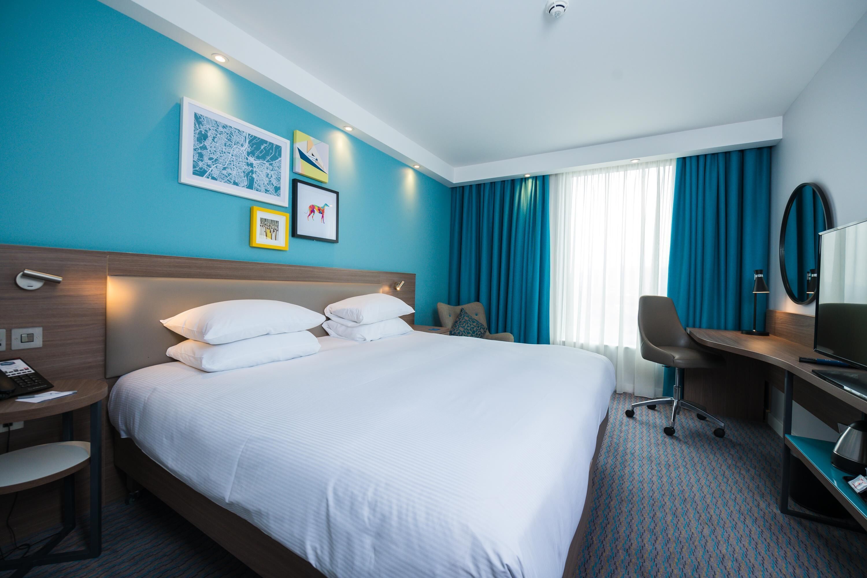 Une chambre d’hôtel avec un grand lit, un bureau avec une chaise, une télévision et des œuvres d’art accrochées au mur.