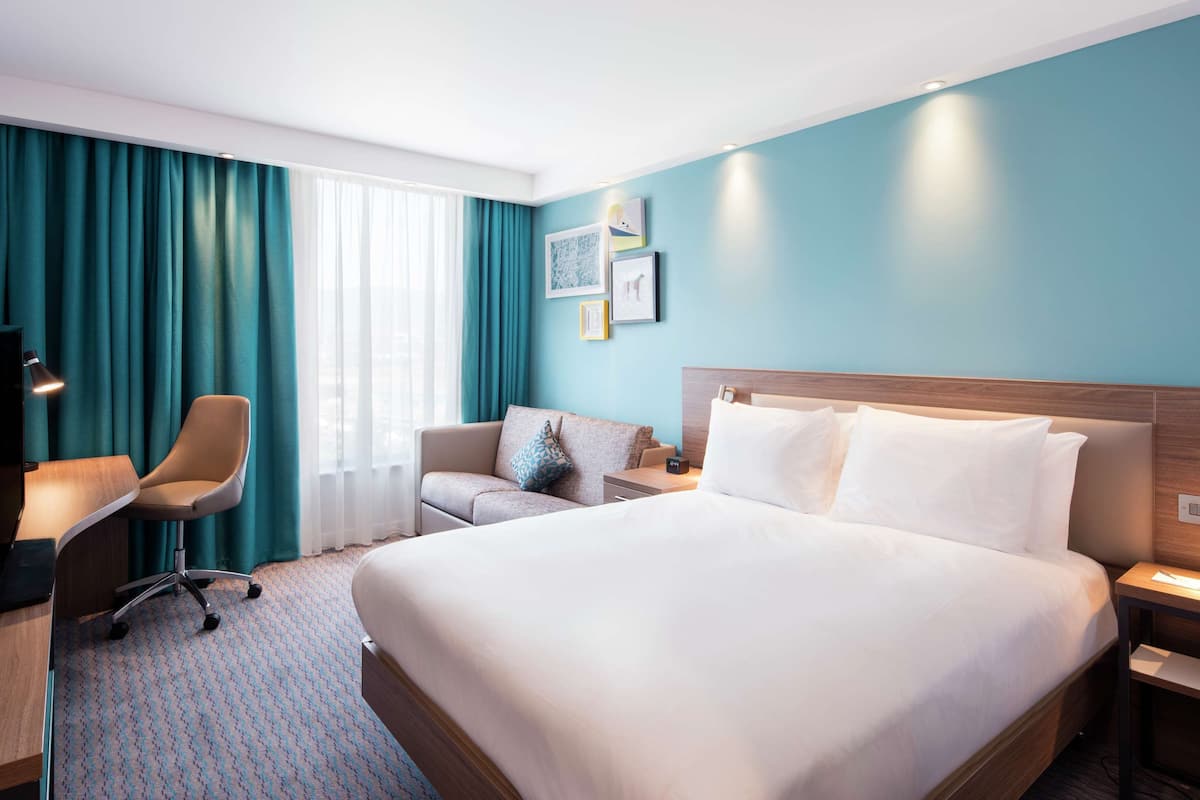 Une chambre d’hôtel avec un grand lit, un bureau avec une chaise, une télévision et une fenêtre avec des rideaux.