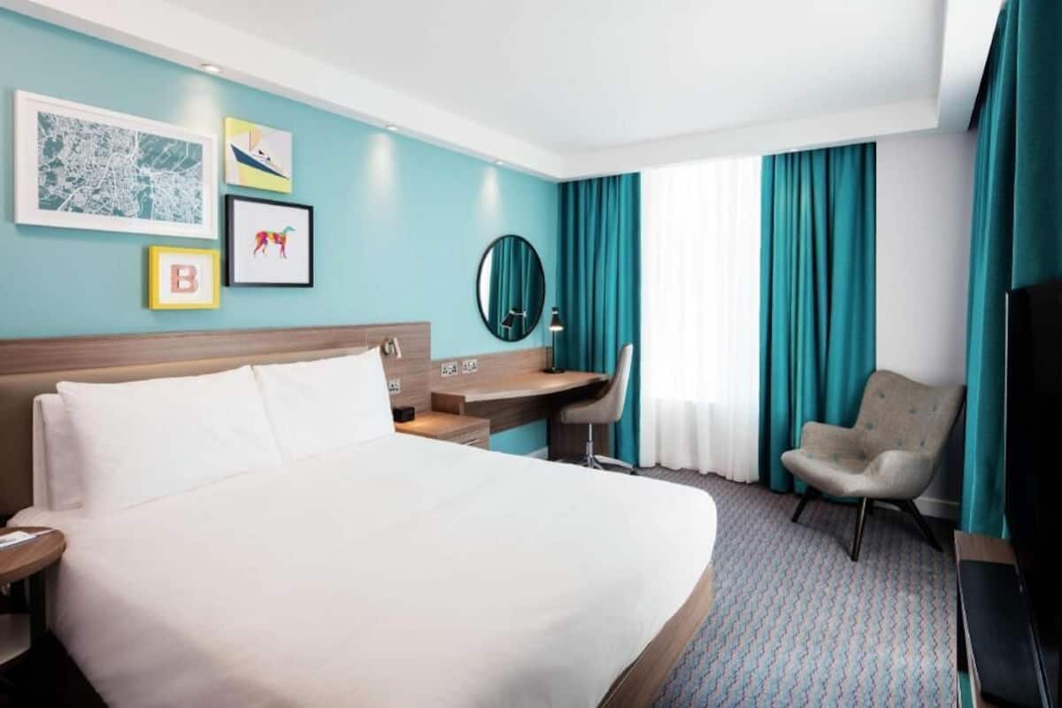 Une chambre d’hôtel équipée d’un lit, d’un bureau, d’une chaise et d’un grand miroir.