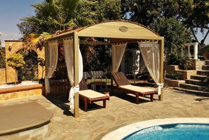 En pavillon med to liggestole, en pool og en stenterrasse.