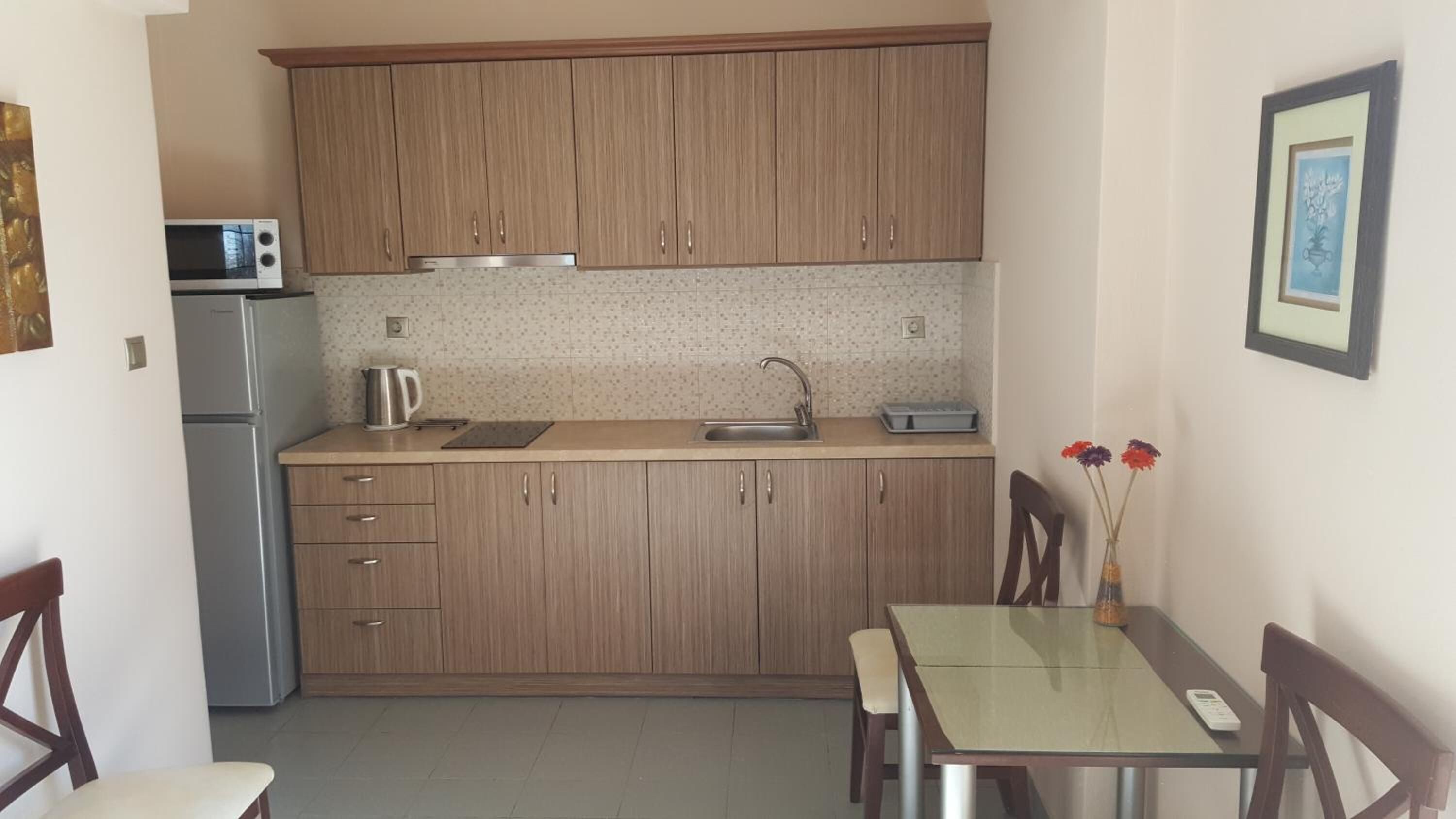 A compact kitchen with wooden cabinets, a microwave, a kettle, and a small dining table with chairs.