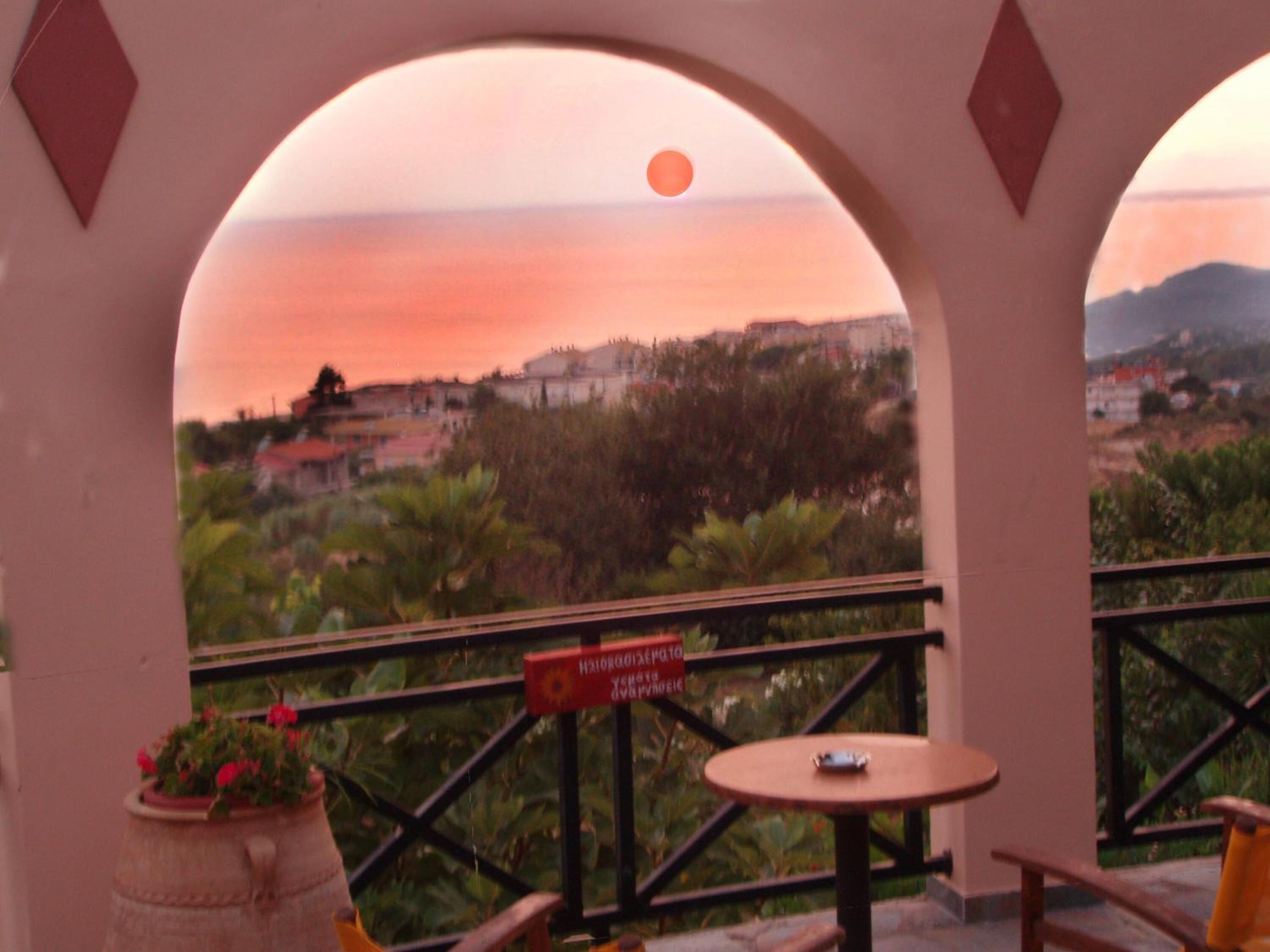 A balcony with a view of a sunset over a hilly landscape, a table with a chair, and a sign with text.