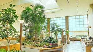 Eine geräumige Lobby mit großen Fenstern, Zimmerpflanzen und einem Empfangsbereich.
