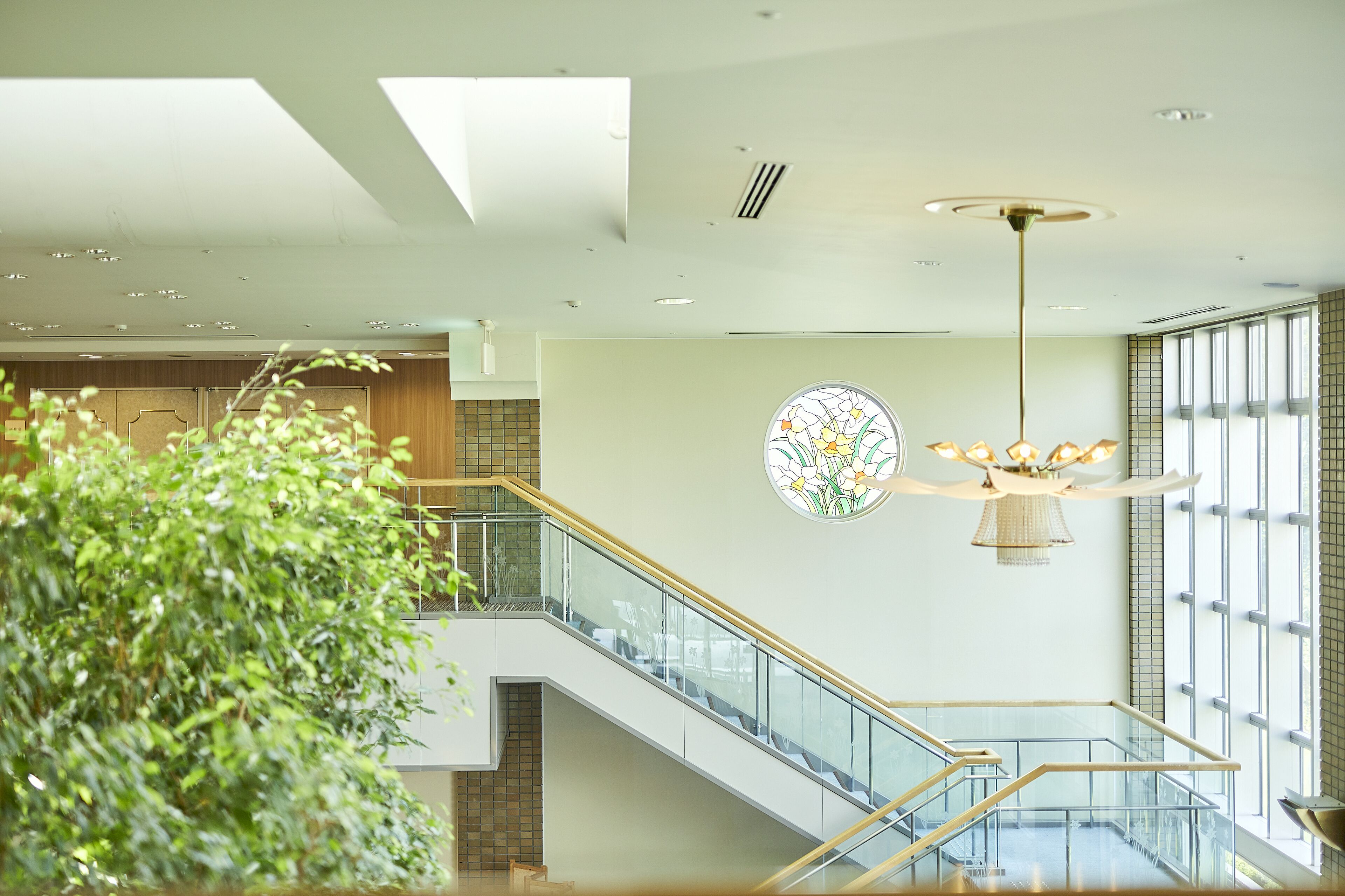 A modern interior with a staircase, a chandelier, and a large window.