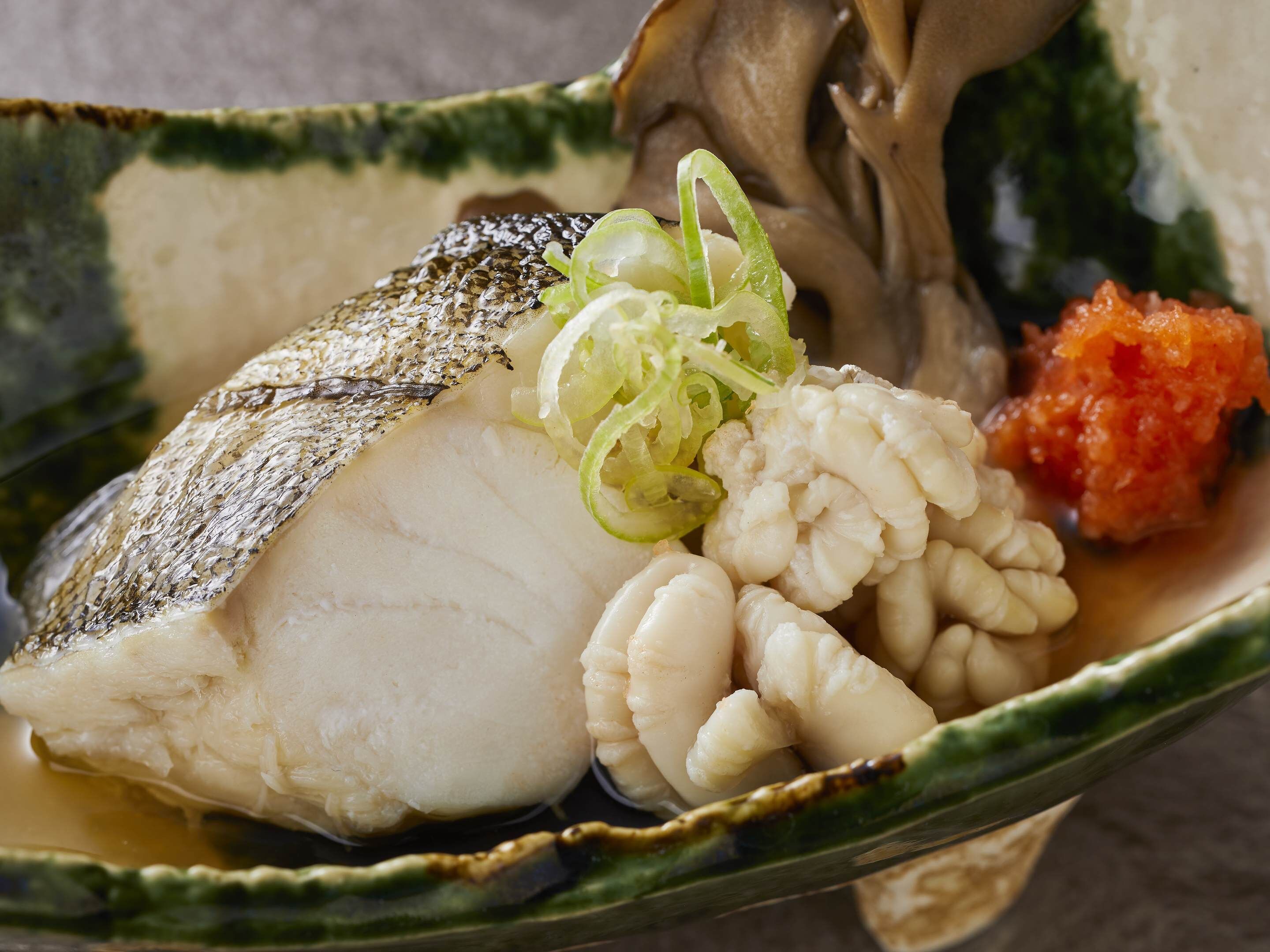 A dish with fish, scallops, and a red sauce in a ceramic bowl.