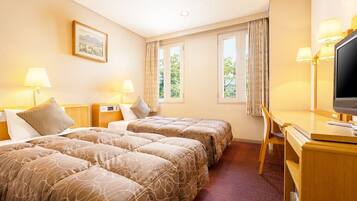 A hotel room with two beds, a desk, a television, and two windows with curtains.